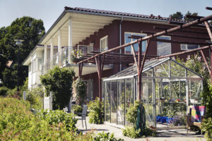 En byggnad i våningar med balkonger, grönska och ett växthus.