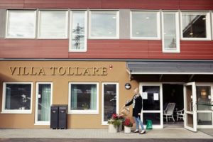 En kvinna vattnar en plantering utanför entrén till Villa Tollare.