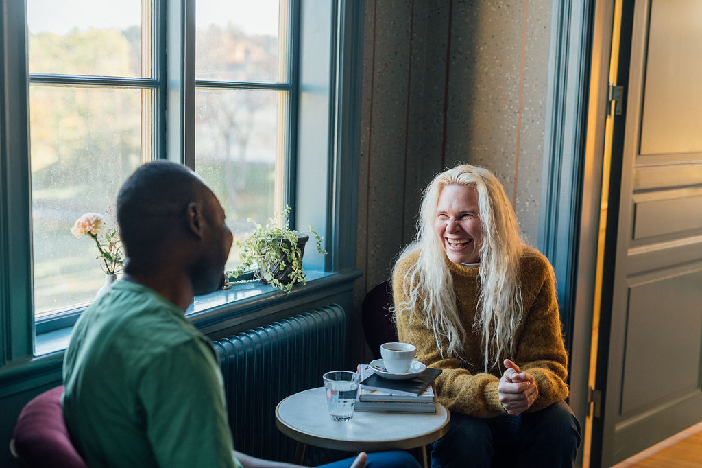 En man och en kvinna, två kollegor, sitter vid ett bord, vid ett fönster och samtalar. De ler och skrattar.