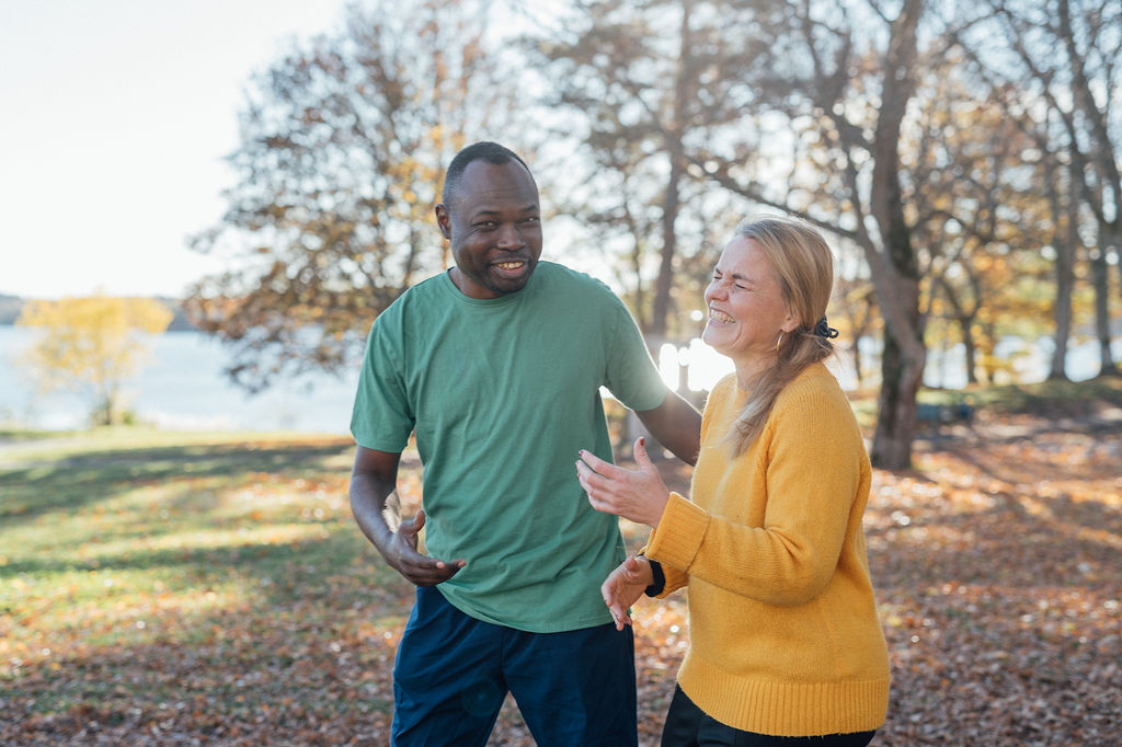 Två medarbetare, en manlig och en kvinnlig, är på promenad ute i skogen. De är glada och skrattar.