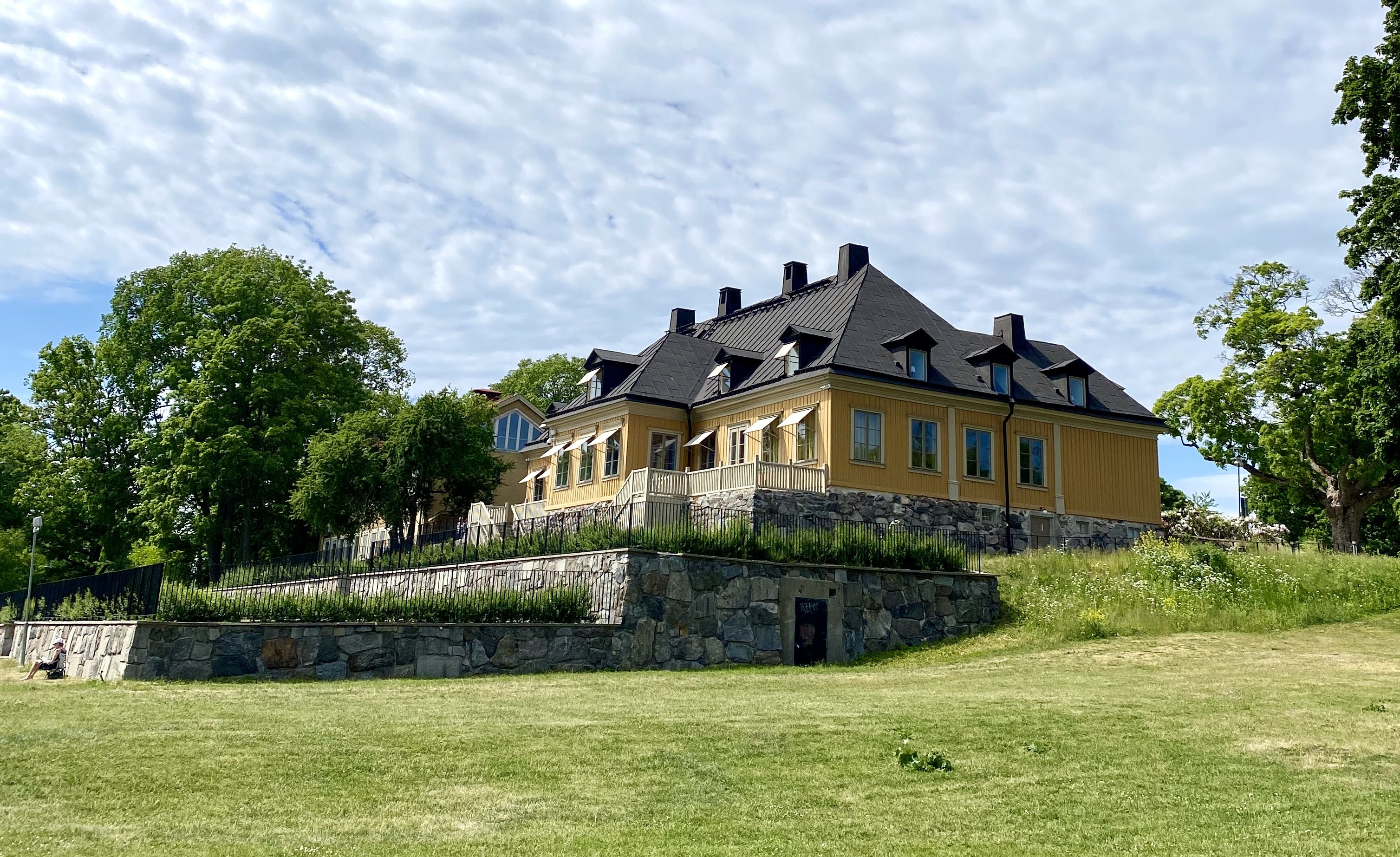 Gult hus på Stora Sköndal i bakgrunden med en grön somrig gräsmatta i förgrunden
