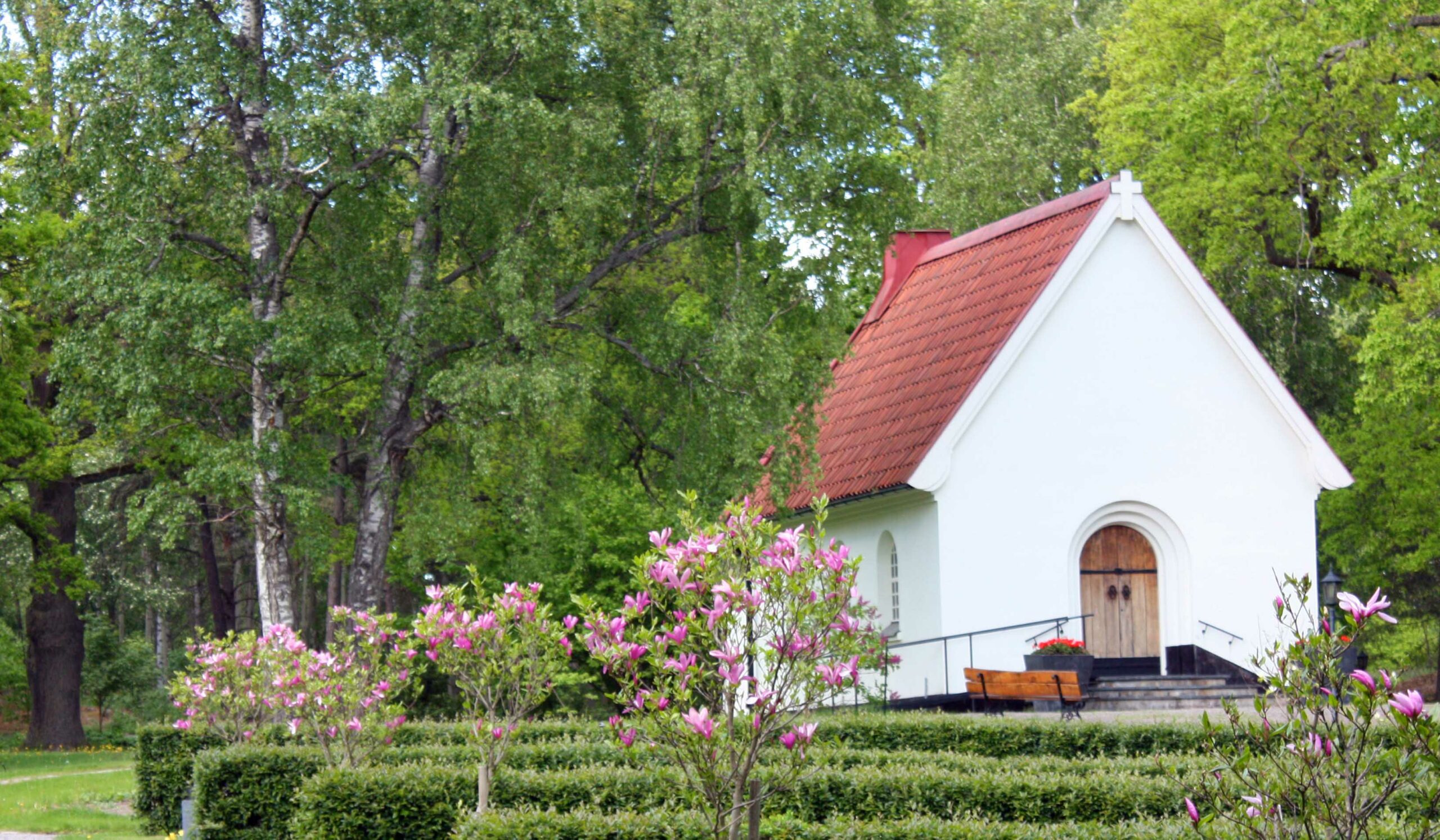 Ett litet vitt kapell på grön kyrkogård.