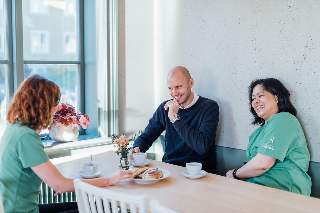 Tre medarbetare sitter vid ett bord och pratar och skrattar.