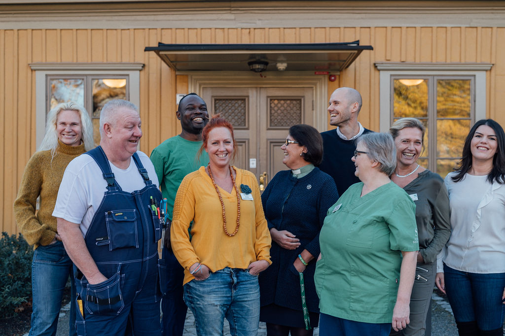 Flera glada medarbetare står tillsammans utanför ett gult hus