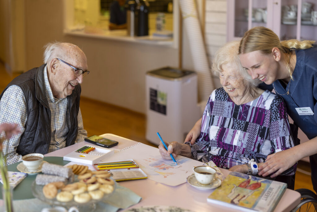 Äldre man och dam ritar och skrattar under fikastunden.