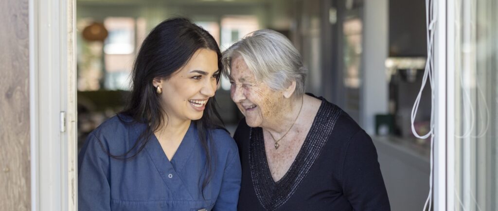 En äldre kvinna lutar sig mot leende kvinna i arbetskläder.