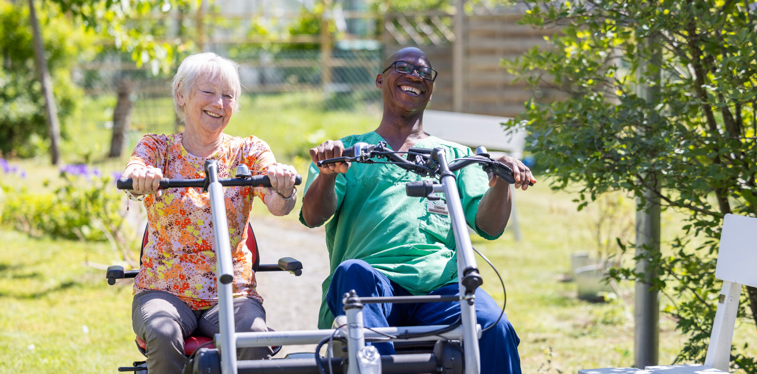 Manlig anställd och äldre kvinna cyklar skrattande på tandemcykel.
