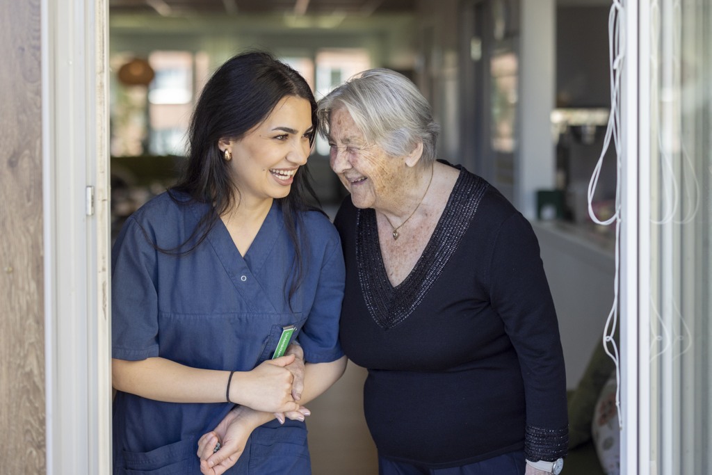 Kvinnlig undersköterska står i en dörröppning med en kvinnlig boende. De skrattar.
