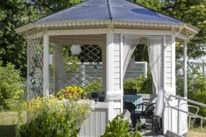 Vitt lusthus omgivet av gröna växter.