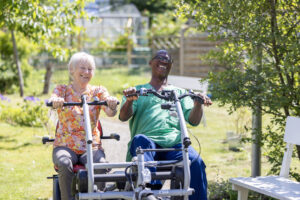 Manlig medarbetare och äldre kvinna cyklar på tandemcykel.